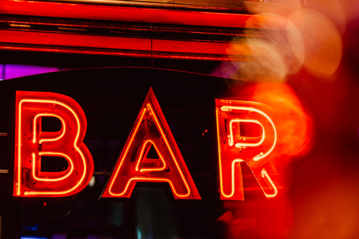 wigilia firmowa spoldzielnia koneser fotograf na impreze 012 Fotorelacja z imprezy firmowej - Żywy czerwony neon z napisem "BAR" na ciemnym tle, z odbiciami i rozmytymi pomarańczowymi światłami tworzącymi żywy, klimatyczny efekt.