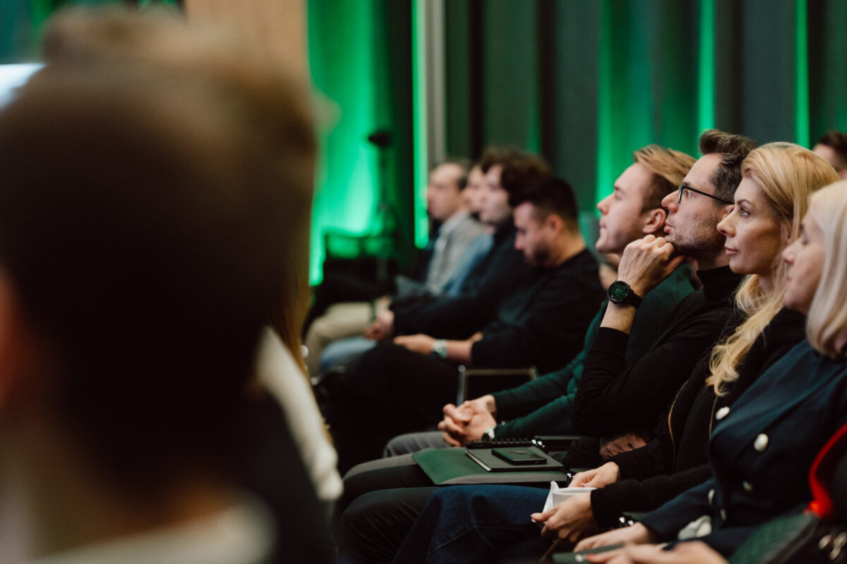 zdjecia eventowe aula polska bnp paribas warszawa 023 Grupa ludzi siedzi w rzędach, słuchając uważnie podczas wydarzenia lub konferencji w pomieszczeniu. Tło jest delikatnie oświetlone zielonym światłem, tworząc skupioną, profesjonalną atmosferę.