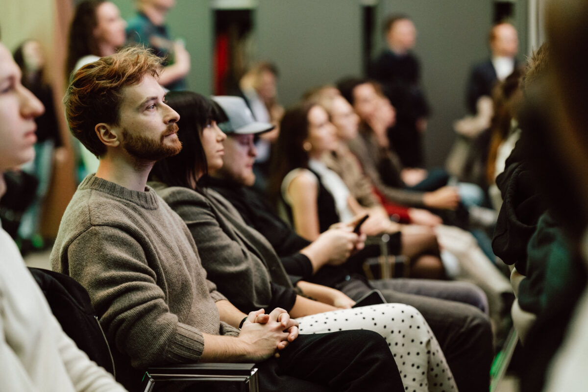 zdjecia eventowe aula polska bnp paribas warszawa 029 Grupa ludzi siedzi blisko siebie na krzesłach, uważnie słuchając prelegenta na imprezie lub konferencji. Większość z nich jest zwrócona do przodu i wygląda na skupionych.