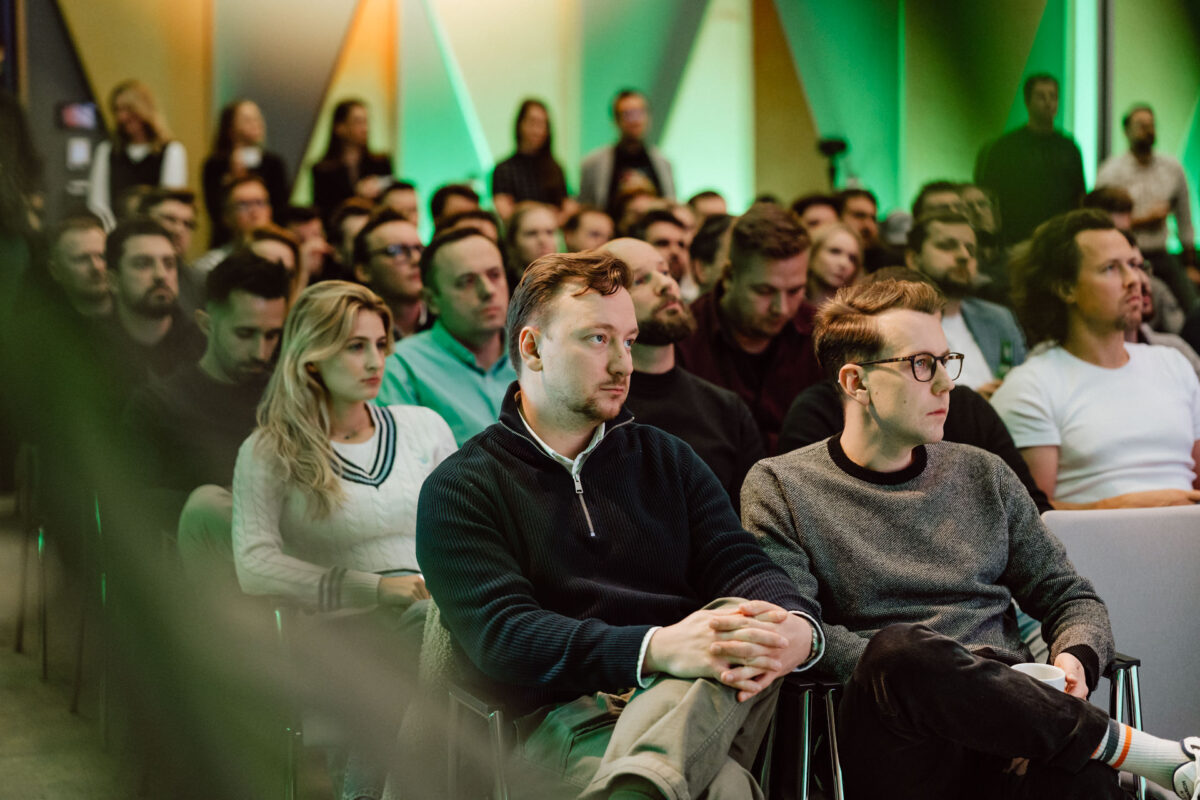 zdjecia eventowe aula polska bnp paribas warszawa 033 Duża grupa ludzi, głównie młodych dorosłych, siedzi blisko siebie w rzędach krzeseł, uważnie słuchając prezentacji lub prelegenta na imprezie wewnętrznej z zielonym i żółtym oświetleniem.