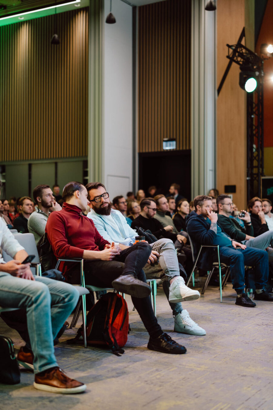 zdjecia eventowe aula polska bnp paribas warszawa 034 Grupa ludzi siedzi w rzędach krzeseł na imprezie lub konferencji w pomieszczeniu. Dwóch mężczyzn na pierwszym planie jest zaangażowanych w rozmowę, podczas gdy inni słuchają uważnie lub patrzą przed siebie.