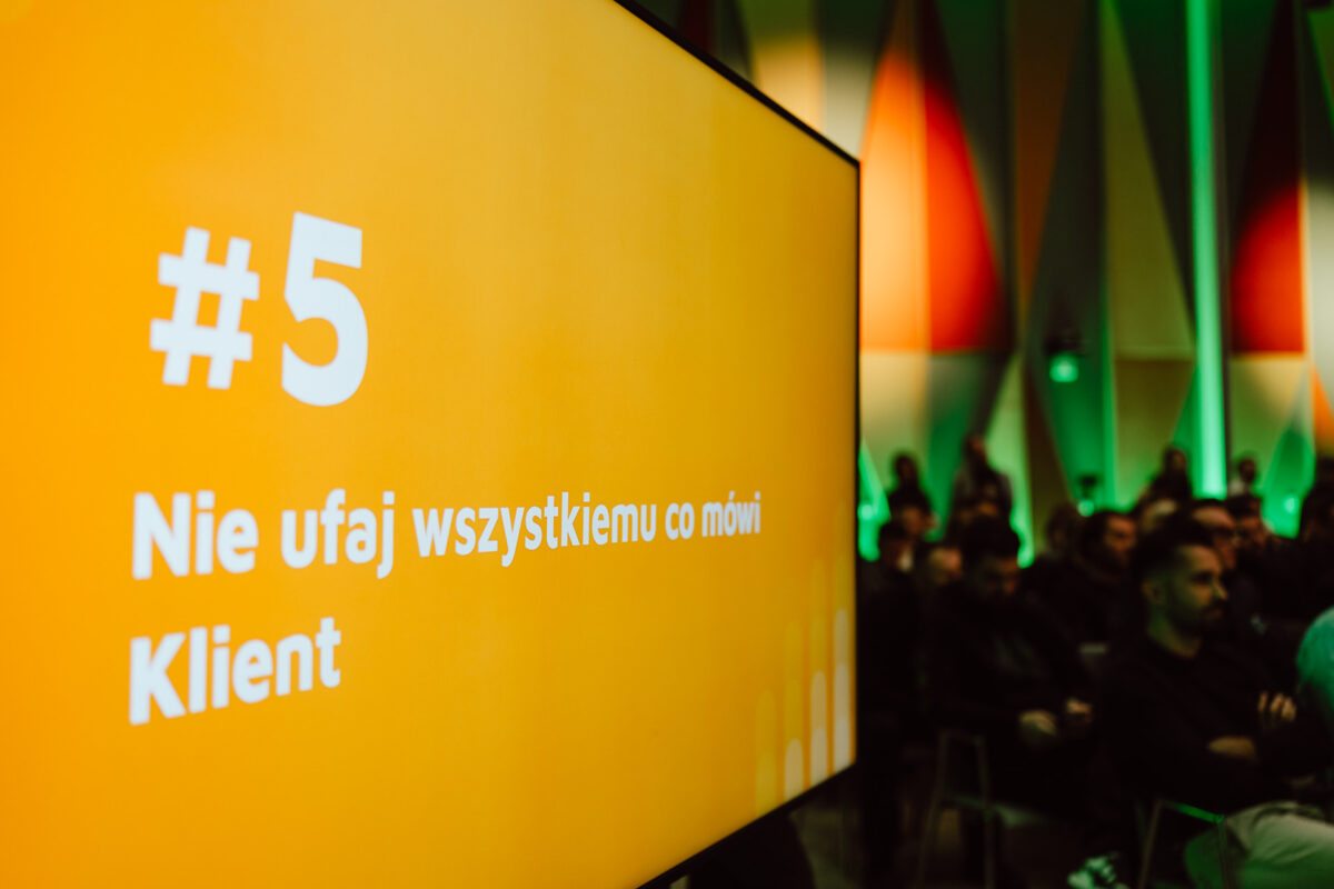 zdjecia eventowe aula polska bnp paribas warszawa 061 Duży żółty ekran wyświetla polski tekst "#5 Nie ufaj wszystkiemu co mówi Klient" przed publicznością w nowoczesnej, kolorowej sali konferencyjnej.