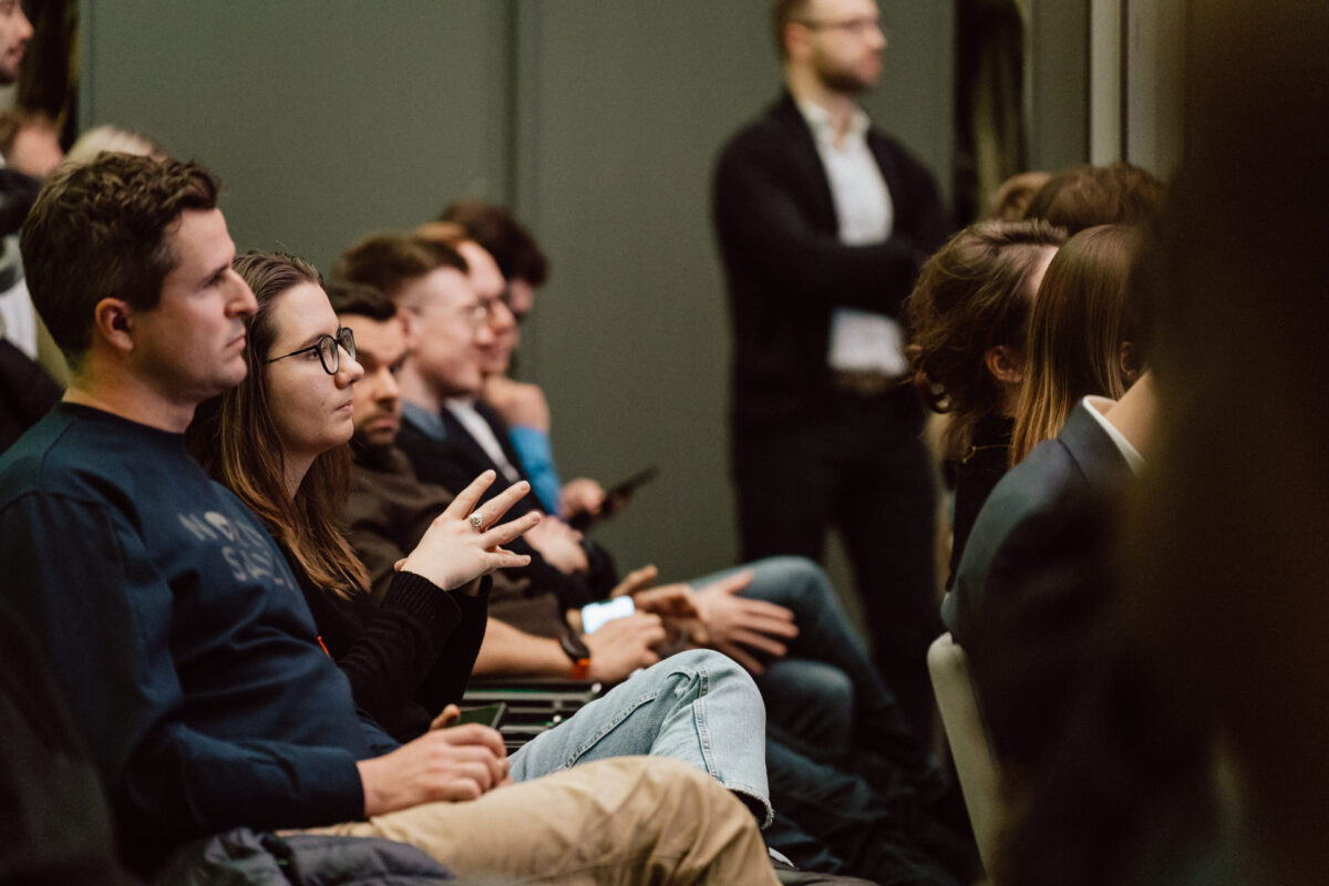 zdjecia eventowe aula polska bnp paribas warszawa 094 Grupa osób siedzących blisko siebie, uważnie słuchających prezentacji lub mówcy. Większość wydaje się skupiona, a niektórzy robią notatki lub trzymają długopisy. Jedna osoba stoi w tle.