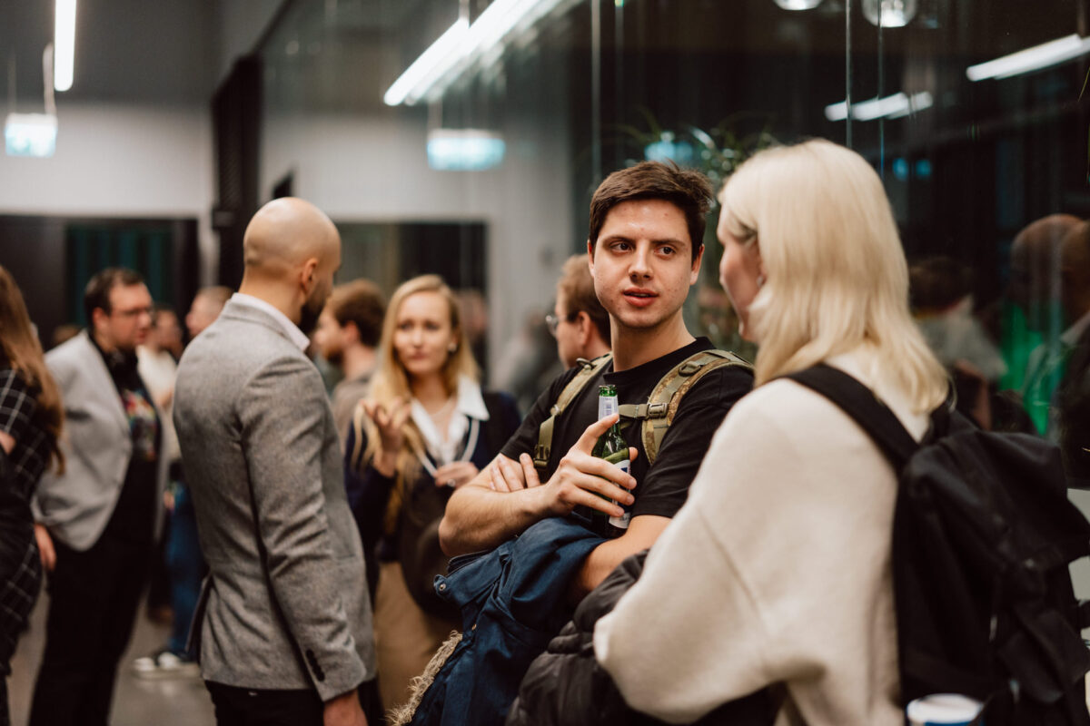 zdjecia eventowe aula polska bnp paribas warszawa 109 Grupa ludzi spotyka się na imprezie wewnątrz budynku. Na pierwszym planie mężczyzna trzymający drinka rozmawia z kobietą. Inni mieszają się i rozmawiają w tle. Atmosfera wydaje się swobodna i przyjazna.