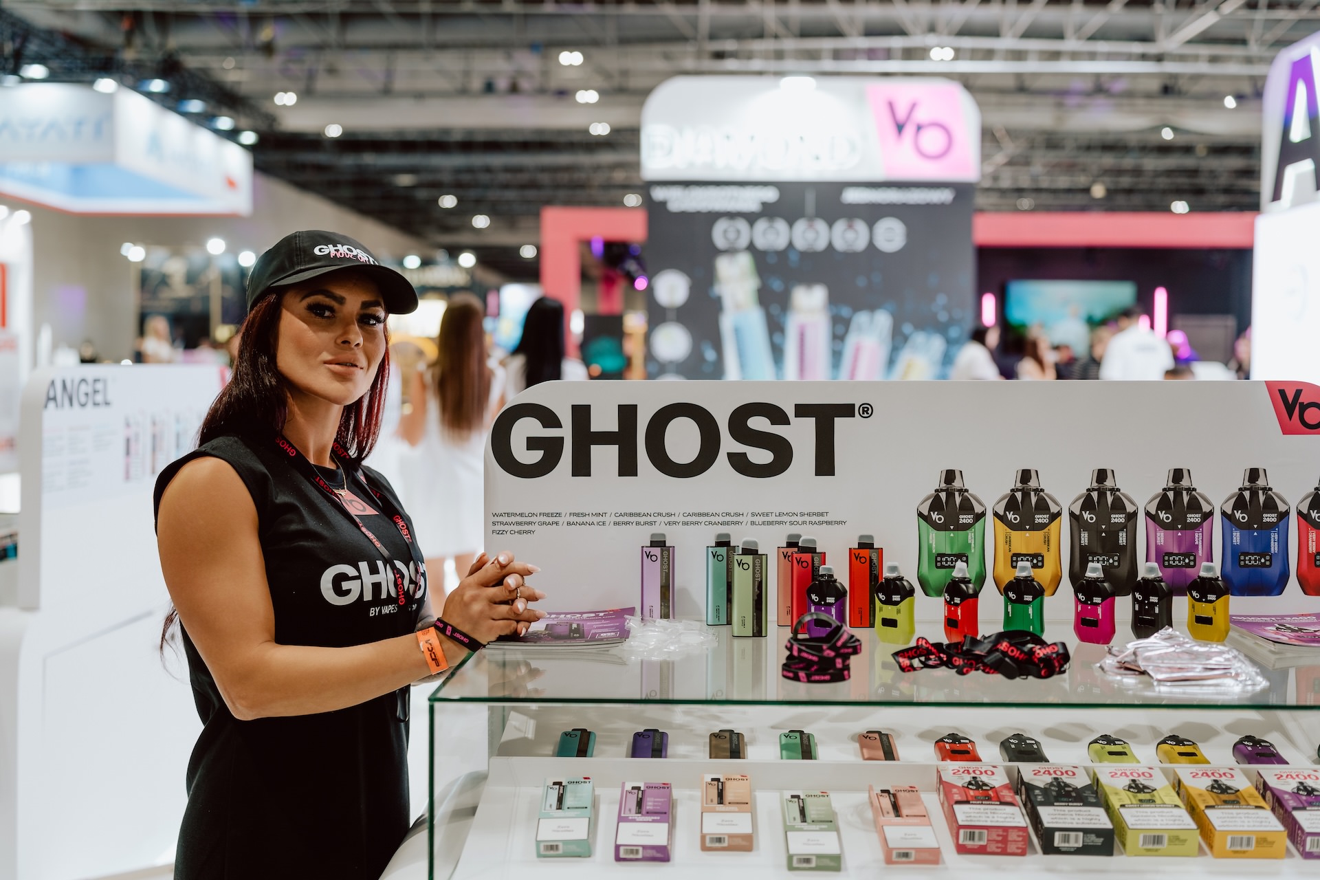 zdjecia live targi vape expo angel Pięć osób w strojach biznesowych stoi w pomieszczeniu, uśmiechając się i gestykulując w kierunku ekranu na stoisku wystawowym. Logo flowair jest widoczne na ekranach w tle, dzięki czemu ta fotografia targowa jest idealna do każdej fotorelacji z targów.