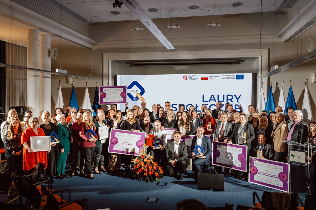 Eine große Gruppe von Menschen posiert zusammen in einem Raum, viele von ihnen halten Urkunden oder Auszeichnungen in der Hand. Hinter ihnen ist ein Bildschirm mit der Aufschrift 'SOCIAL AWARDS' zu sehen. Es sieht aus wie eine Preisverleihung oder eine offizielle Veranstaltung.  