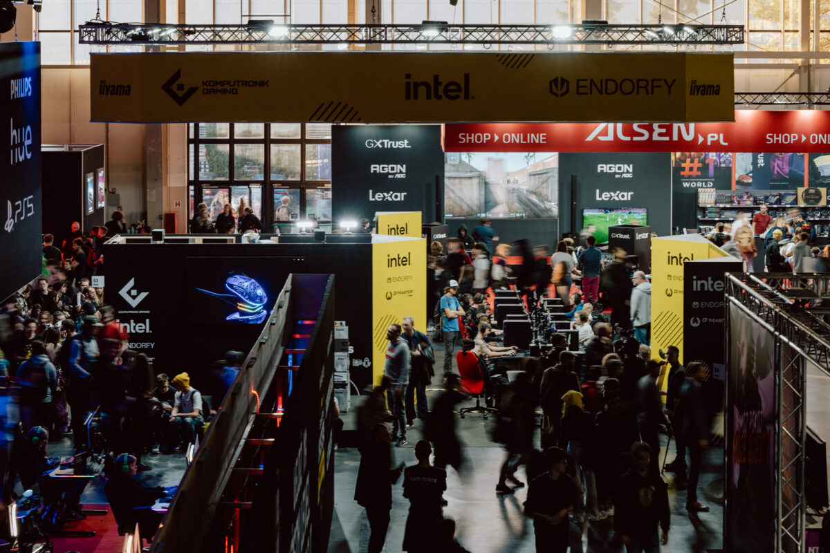 Eine geschäftige Spieleveranstaltung mit vielen Menschen, die um die Stände herumlaufen und sich versammeln. Verschiedene Banner und Firmenlogos sind zu sehen, darunter Intel und ENDORFY. Die Atmosphäre wird durch die Menschenmenge und die beleuchteten Displays belebt.  