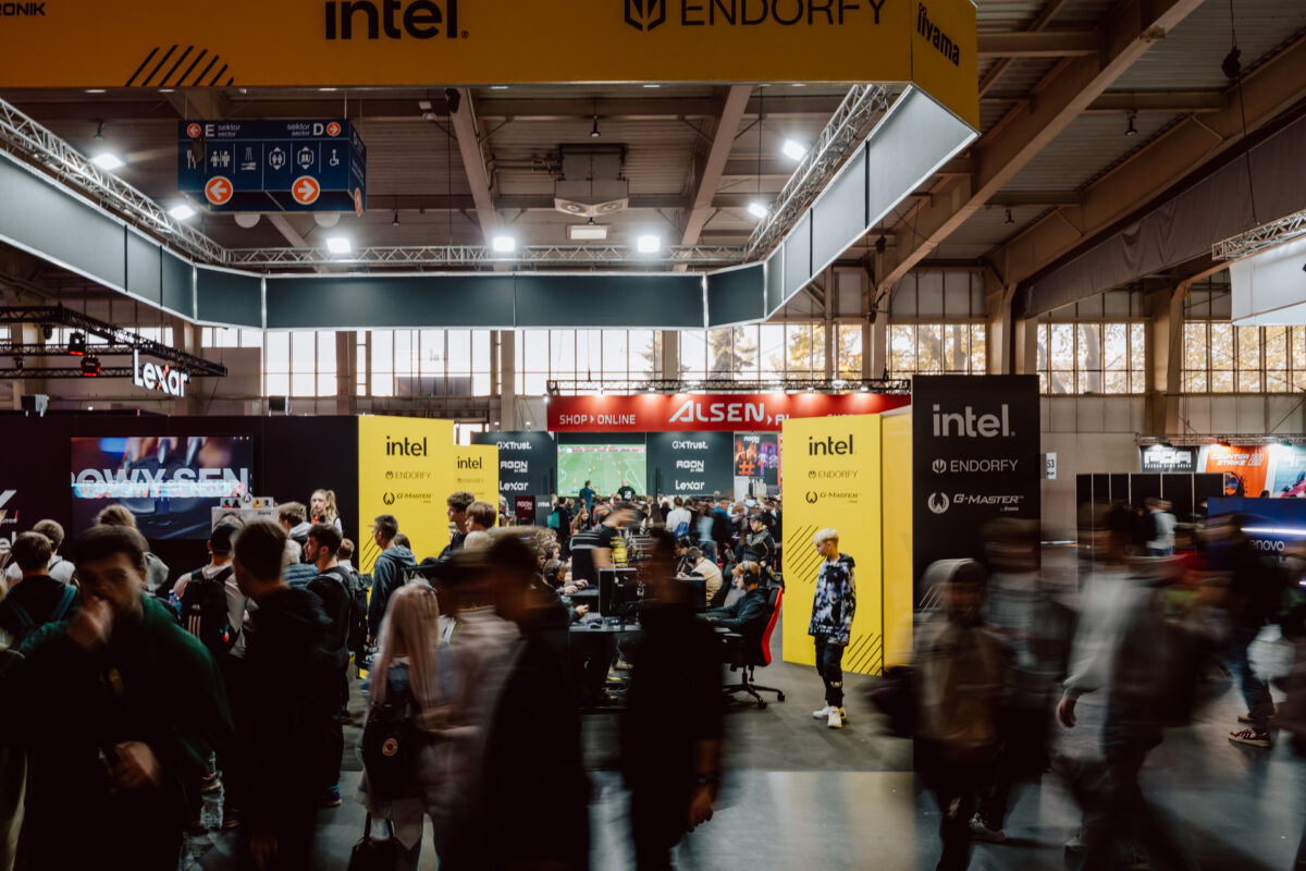 Eine belebte Kongresshalle mit Menschen, die an einem Stand mit Bannern von Intel und Endorfa vorbeilaufen. Helle Lichter erhellen den Bereich und hinter der Menge sind Computermonitore zu sehen. 