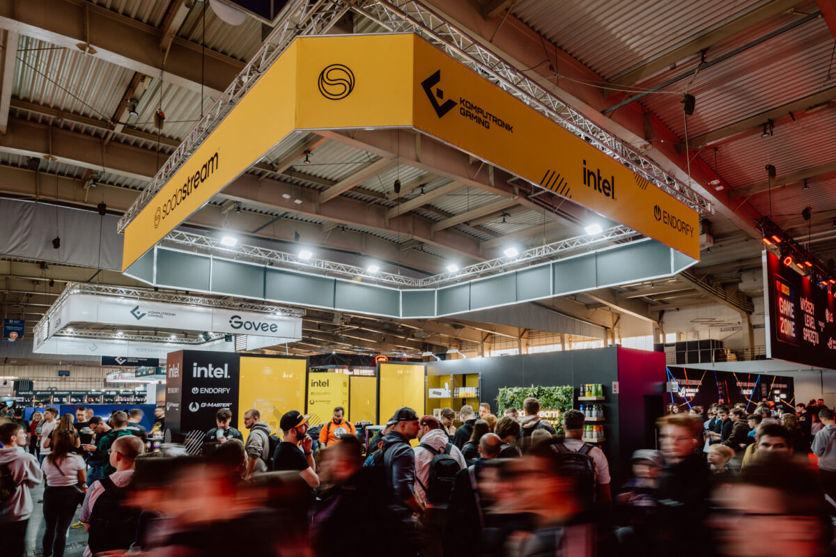 Eine große Menschenmenge besucht den Technologiekongress in einer geräumigen Halle mit hell erleuchteten Ständen von Unternehmen wie Intel, Govee und Ducky unter gelben Bannern und Deckenleuchten im industriellen Stil.