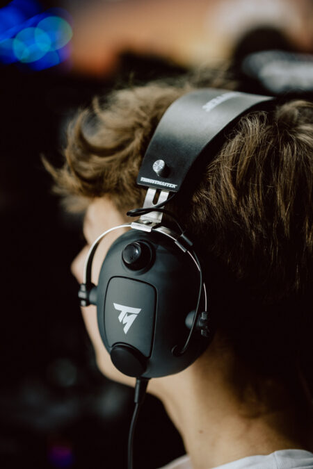 Eine Person mit braunem Haar, die große schwarze Gaming-Kopfhörer trägt, von der Seite und leicht von hinten gesehen, mit einem unscharfen Hintergrund.