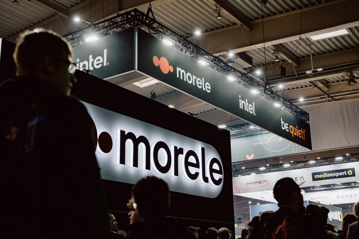 Eine große Menschenmenge versammelt sich auf der Technologiemesse. Über und um den Messestand herum hängen beleuchtete "Morele"-, "Intel"- und "Be quiet!"-Schilder.