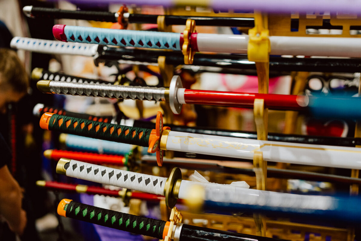 Auf dem Ständer stehen mehrere bunte Katana-Schwerter mit unterschiedlich gemusterten Griffen und Scheiden, die horizontal in Reihen angeordnet sind.