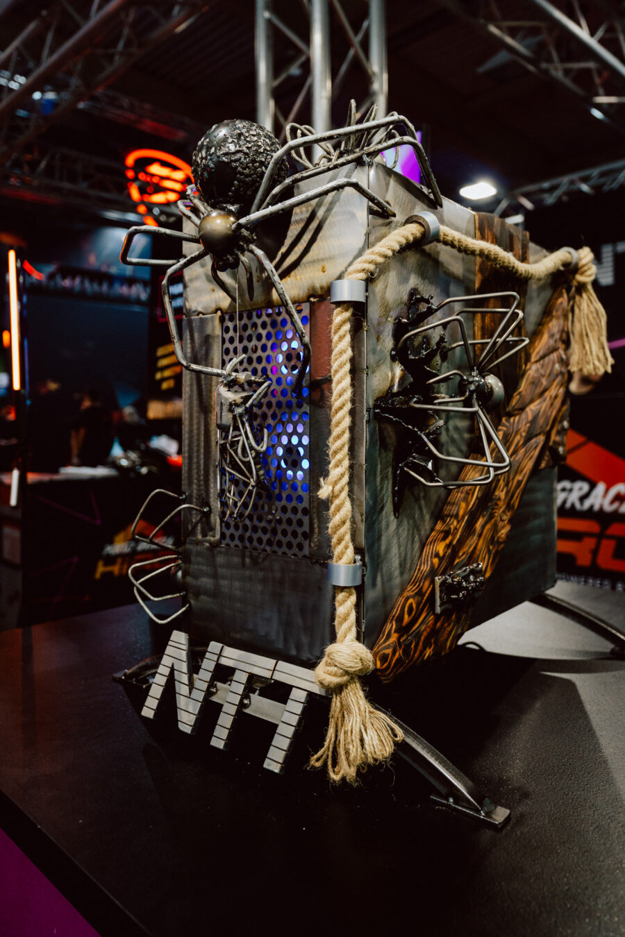 Ein speziell angefertigtes Computergehäuse, das mit großen schwarzen Spinnen, Seilen und Metallakzenten verziert ist, mit beleuchteten blauen Lüftern im Inneren und den Buchstaben 'NTT' am Sockel.