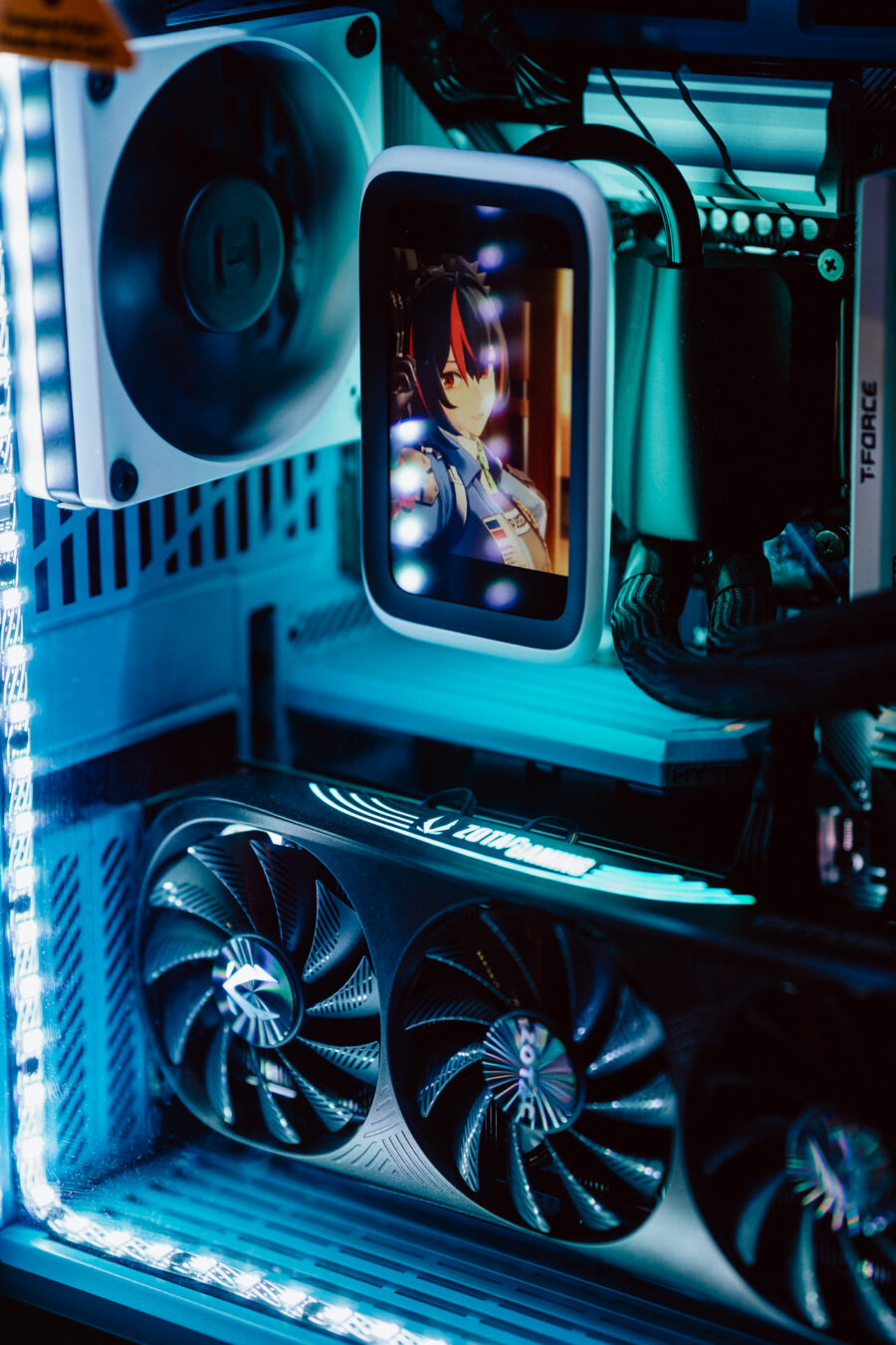 Nahaufnahme eines kundenspezifischen PCs mit blauer LED-Beleuchtung, sichtbaren Lüftern und einem kleinen Bildschirm im Inneren des Gehäuses, der eine Anime-Figur darstellt.