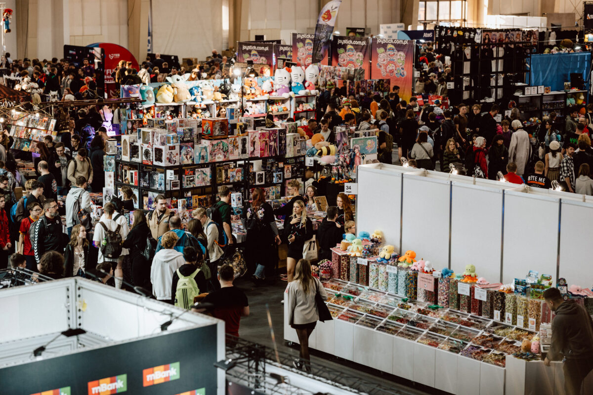 Eine überfüllte Kongresshalle mit Menschen, die sich an den verschiedenen Ständen der Verkäufer von Spielzeug, Teddybären, Sammlerstücken und bunten Waren umsehen. Die Atmosphäre ist lebhaft und hektisch. 