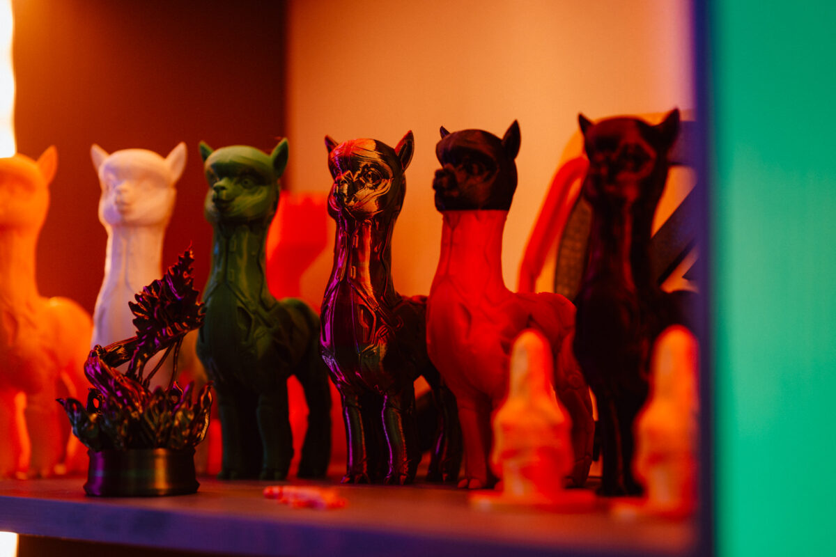 Eine Reihe bunter Lama-Figuren, darunter weiße, grüne, lila und rote, die auf einem Regal mit warmer und kühler Beleuchtung ausgestellt sind. Auf dem Regal befinden sich auch andere kleine Dekorationsartikel. 