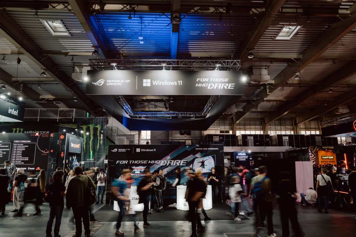Menschenmassen laufen durch die große Ausstellungshalle mit Bannern von Windows 11 und Republic of Gamers über ihren Köpfen, während im Hintergrund verschiedene Stände und Displays beleuchtet sind.