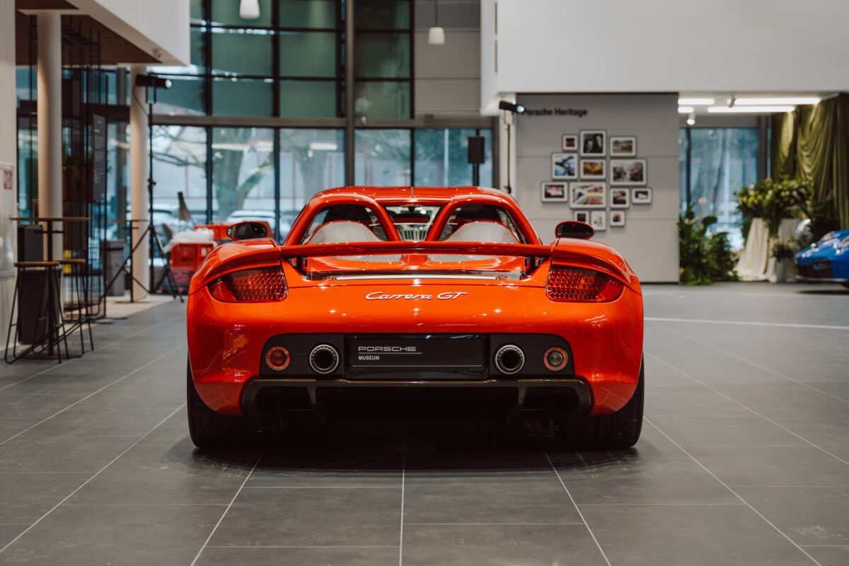 Der leuchtend rote Porsche Carrera GT Sportwagen ist von innen zu sehen, von hinten gesehen, mit seinen charakteristischen Doppelauspuffanlagen, Rückleuchten und der 'Carrera GT'-Plakette, die im modernen Showroom bei der Eröffnung des Ausstellungsraums zu sehen ist.