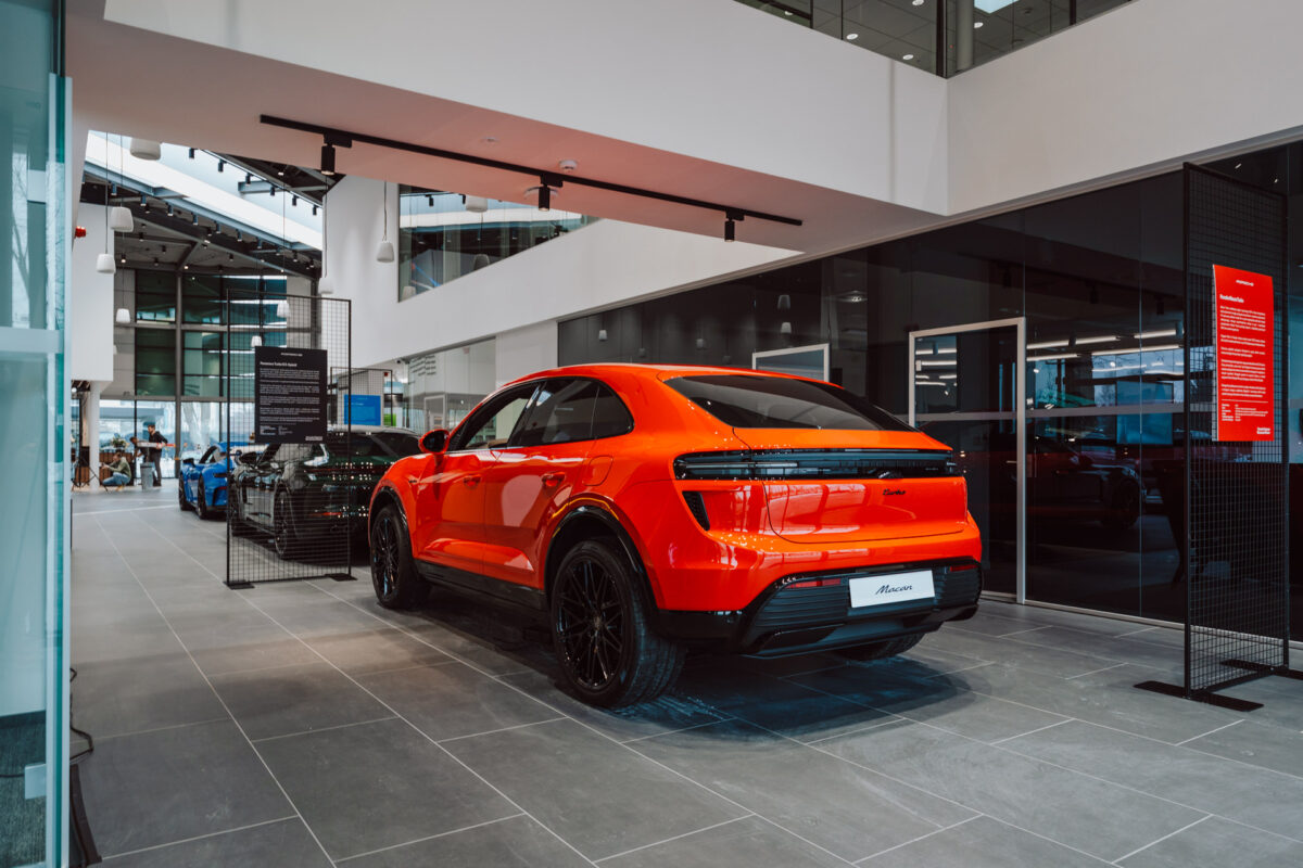 Der leuchtend orangefarbene SUV wird in einem modernen Autohaus mit großen Fenstern und einem schlichten, minimalistischen Innendesign präsentiert, bereit für die Eröffnung des Showrooms.