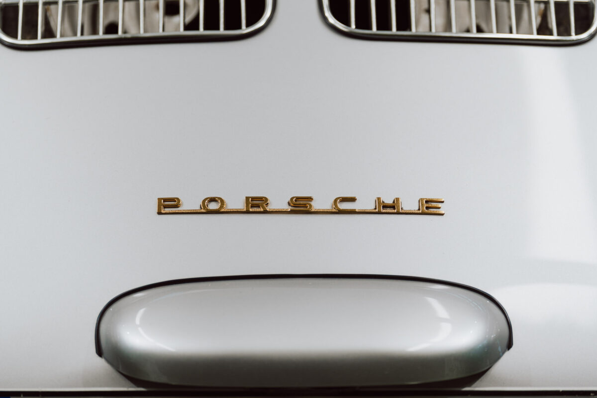 Nahaufnahme der Vorderseite des klassischen silbernen Porsche, die das goldene Porsche-Emblem und einen Teil der Motorhaube mit zwei verchromten Lüftungsöffnungen zeigt - eine elegante Wahl für jede Ausstellungseröffnung.