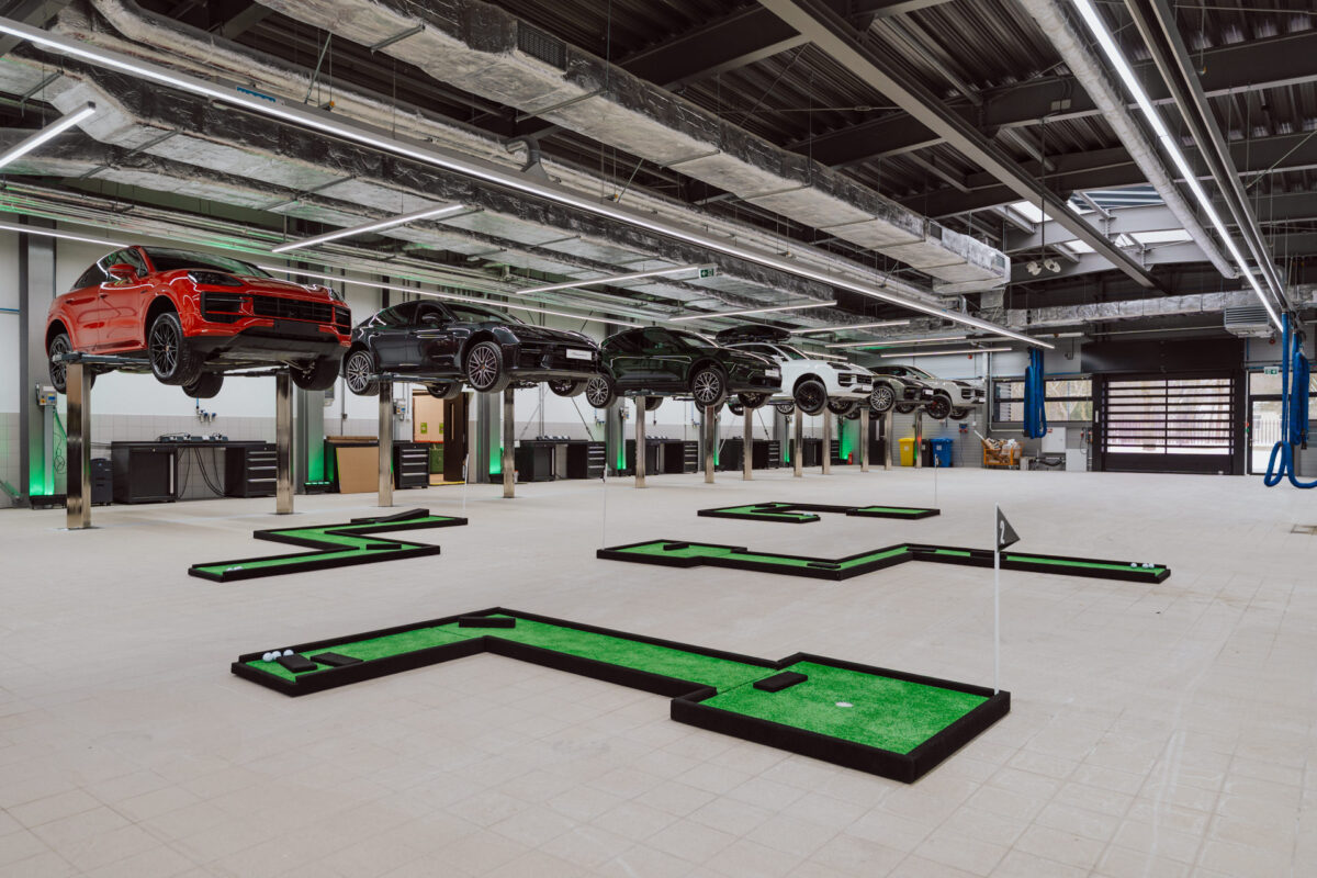 Ein geräumiger Innenbereich mit Autos, die auf Liften über Minigolf-Löcher und grünen Rasen gehoben werden. So entsteht ein einzigartiger Minigolfplatz zum Thema Auto - perfekt für die Eröffnung eines Showrooms.