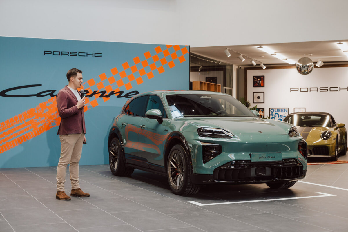 Bei der Eröffnung des Showrooms steht ein Mann neben einem türkisfarbenen Porsche Macan Elektro-Geländewagen im Showroom, während im Hintergrund ein blauer und oranger Porsche Cayenne und ein weiterer Porsche Sportwagen zu sehen sind.