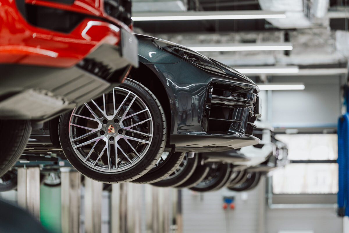 Die Autos werden in einer modernen Autowerkstatt auf Hebebühnen gehoben. Ein dunkel gefärbtes Auto und seine Aluminiumfelge stehen im Mittelpunkt, während andere Fahrzeuge bei der Eröffnung des Showrooms in hellem Licht zu sehen sind. 