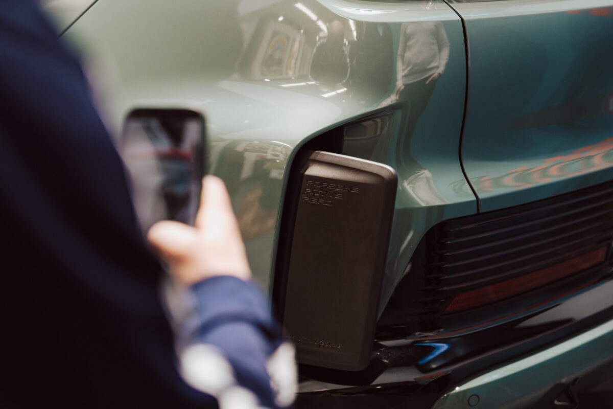 Eine Person hält ein Smartphone in die Nähe des Rücksitzes eines grünen Porsche und konzentriert sich dabei auf den Ladeanschluss und das Rücklicht des Fahrzeugs - und fängt damit die Spannung der Eröffnung des Ausstellungsraums für Elektrofahrzeuge ein.