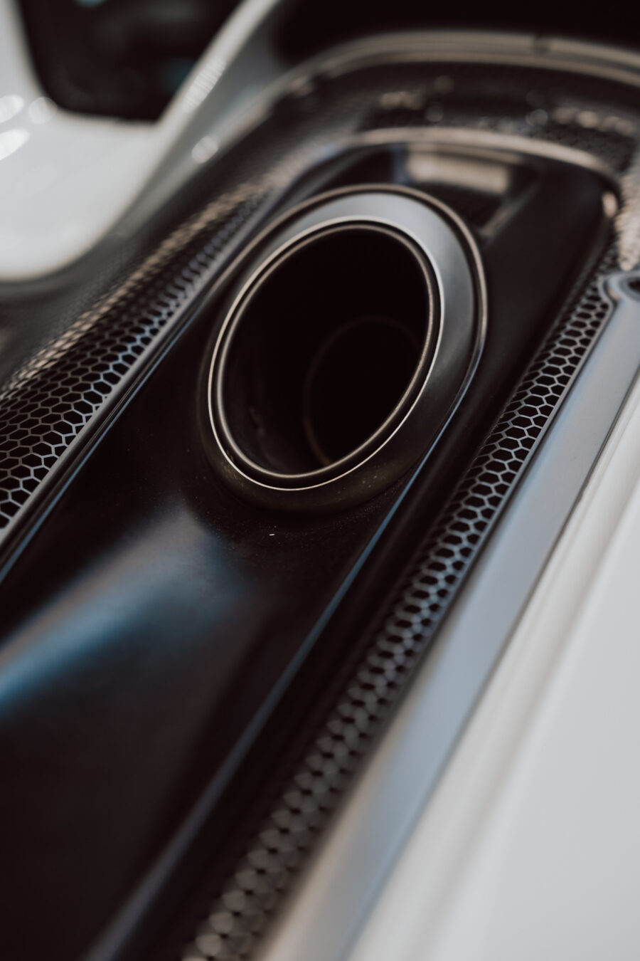 Nahaufnahme des Auspuffrohrs des Autos mit einem eleganten, modernen Look, ideal für die Präsentation in einem offenen Ausstellungsraum, umgeben von schwarzem Netz und glatten Metalloberflächen.