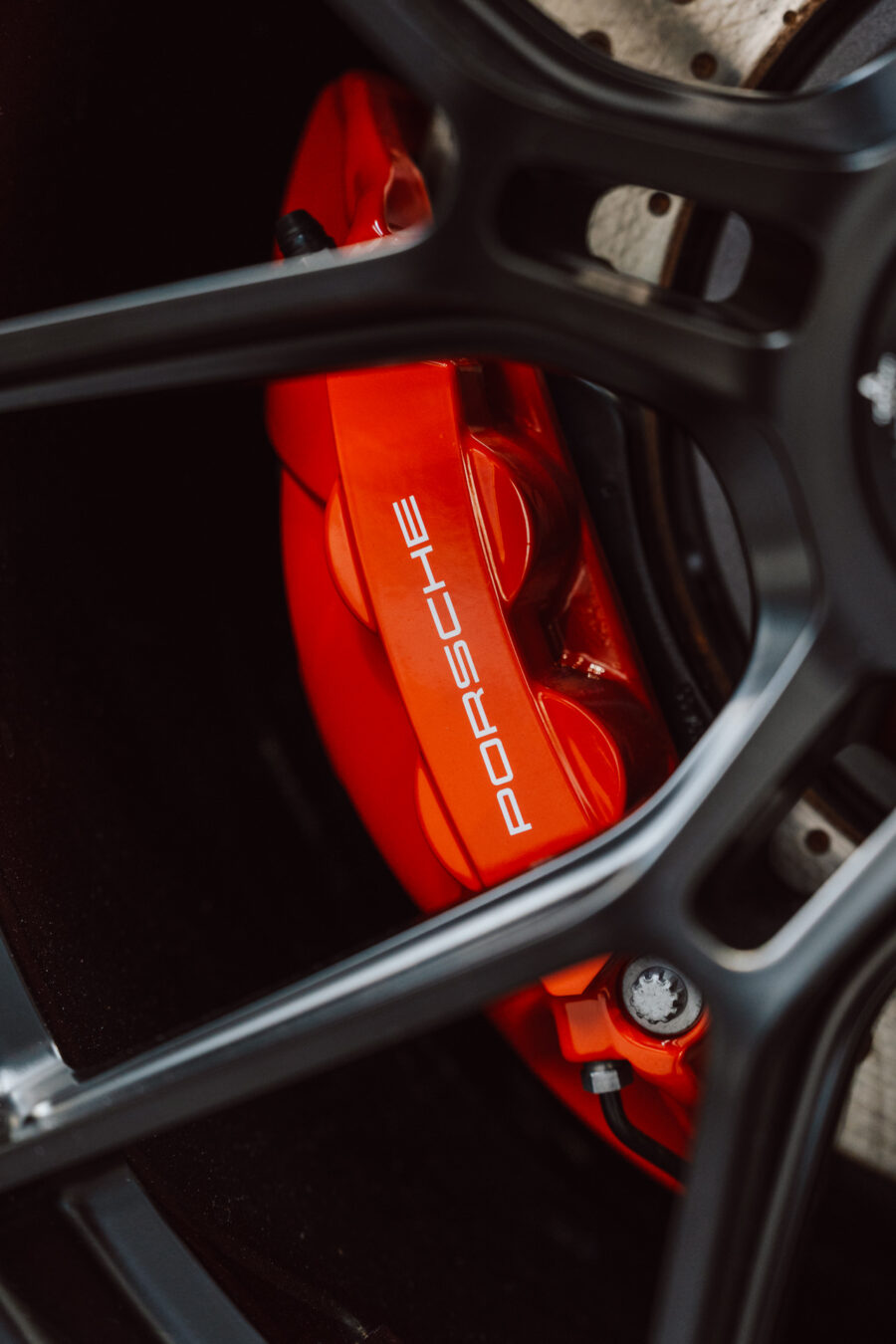 Nahaufnahme des roten Porsche Bremssattels hinter dem schwarzen Leichtmetallrad. Der Porsche Schriftzug auf dem Bremssattel ist deutlich sichtbar - aufgenommen während der Eröffnung des Showrooms.