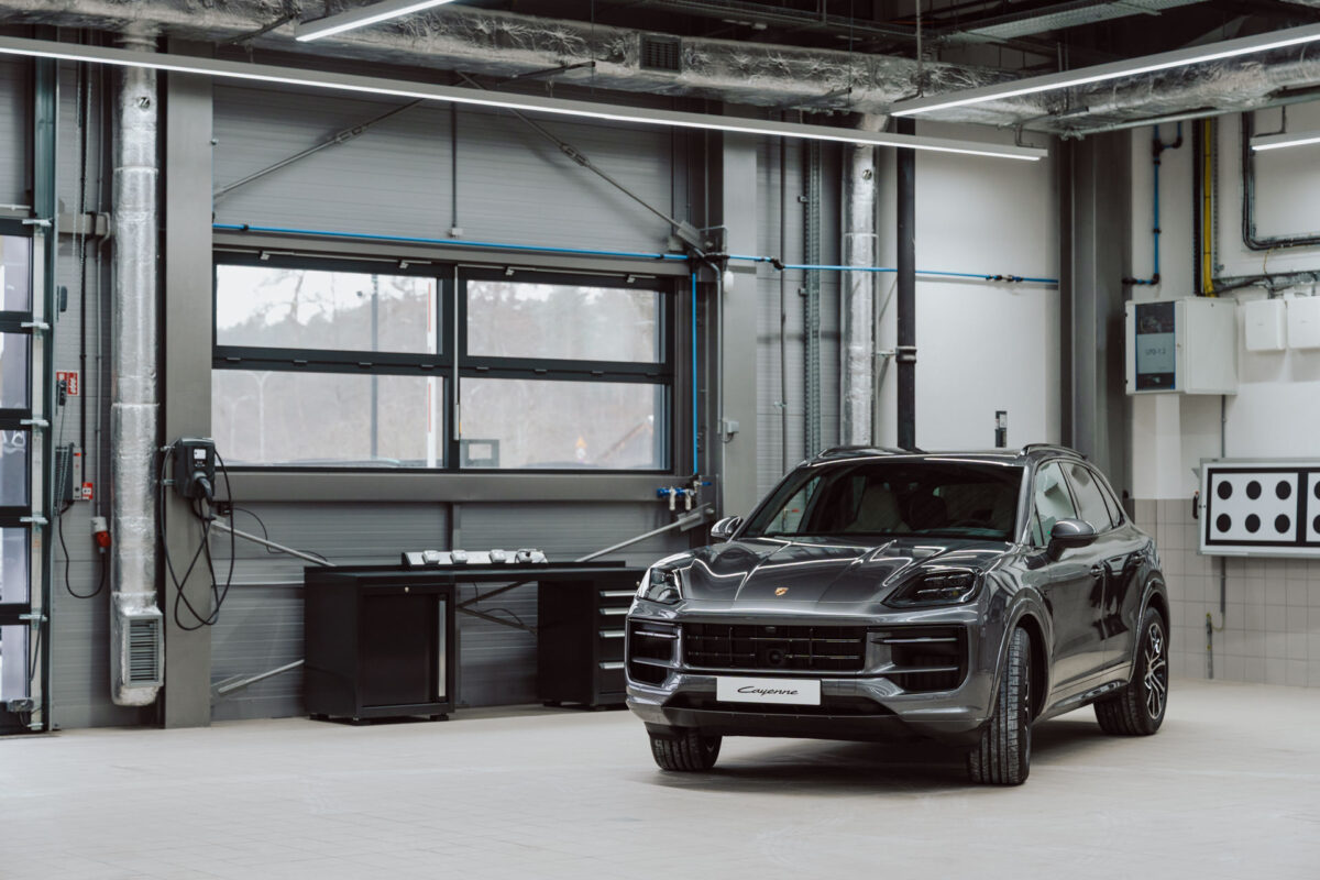 Der schwarze Porsche Cayenne SUV steht in einer geräumigen, modernen Industriegarage mit großen Fenstern und freiliegenden Rohren, die so angeordnet sind, dass sie den Ausstellungsraum mit verschiedenen Geräten an den Wänden öffnen.