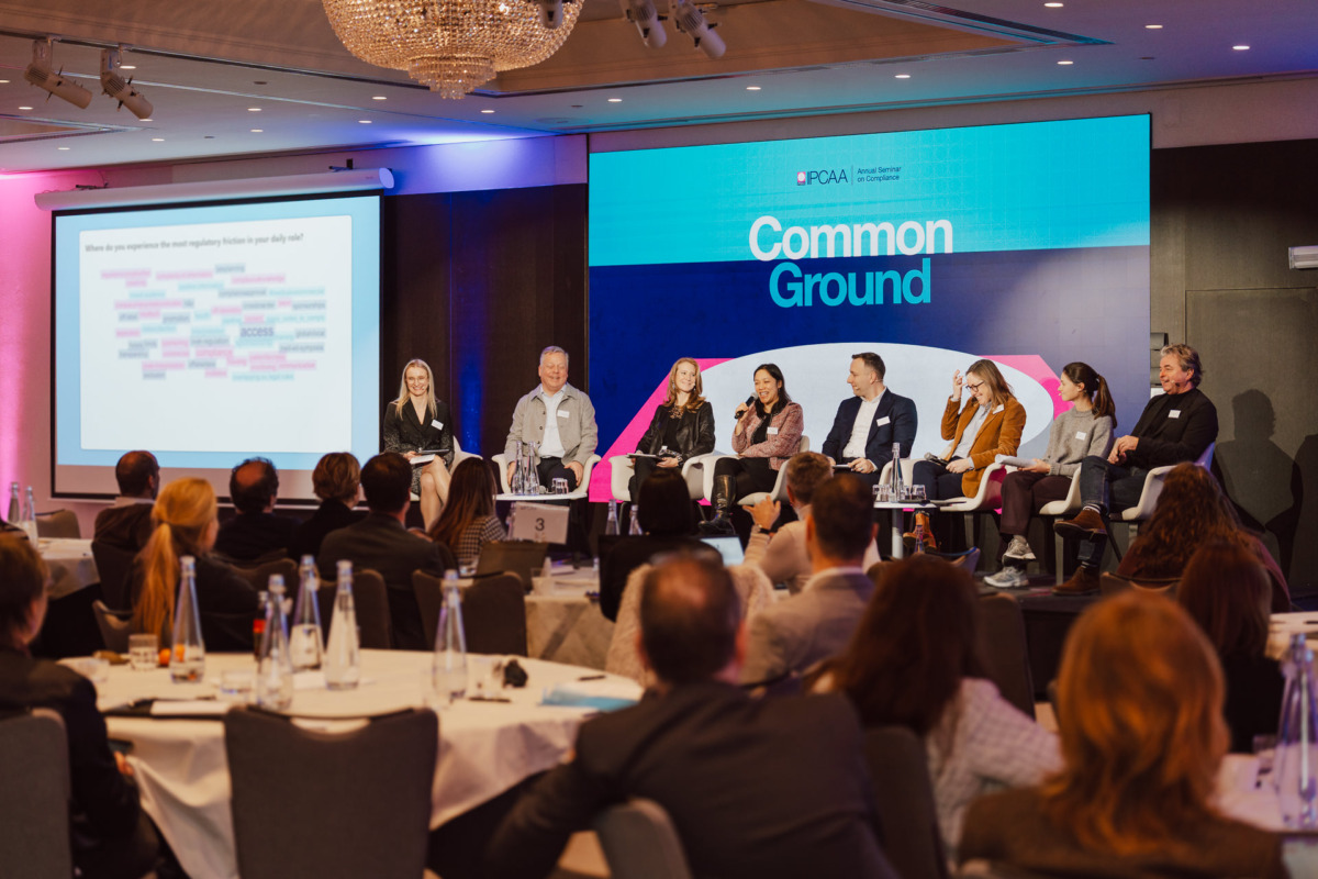 Panel ośmiu osób siedzi na scenie z mikrofonami podczas konferencji, przed publicznością. Na dużym ekranie wyświetlana jest chmura słów i napis "Common Ground". Otoczenie to nowoczesna sala konferencyjna.
