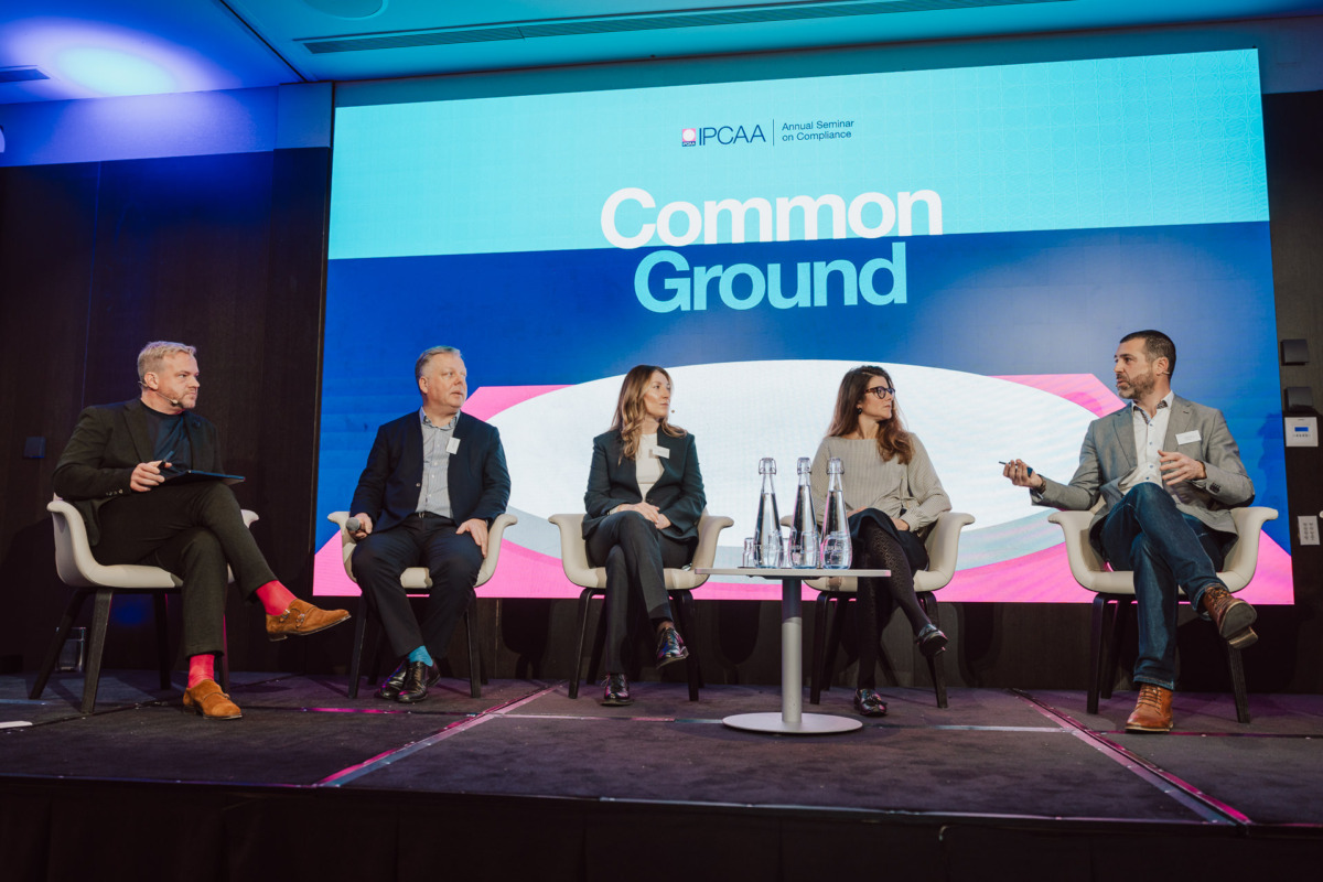Pięć osób siedzi na scenie panelu dyskusyjnego przed ekranem wyświetlającym "Common Ground" podczas dorocznego seminarium PCAA. Trzech mężczyzn i dwie kobiety prowadzą rozmowę, siedząc na białych krzesłach.