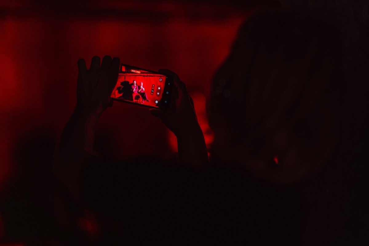 Widzka nagrywa telefonem występ w czerwonym świetle sceny