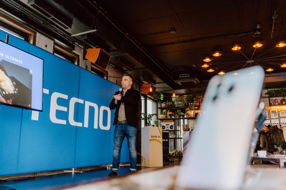 Wystąpienie na tle ścianki Tecno podczas premiery smartfona, telefon na pierwszym planie