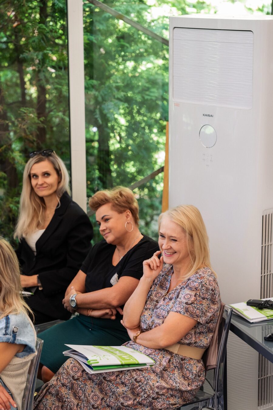 Trzy uśmiechnięte uczestniczki konferencji z broszurami programu na widowni