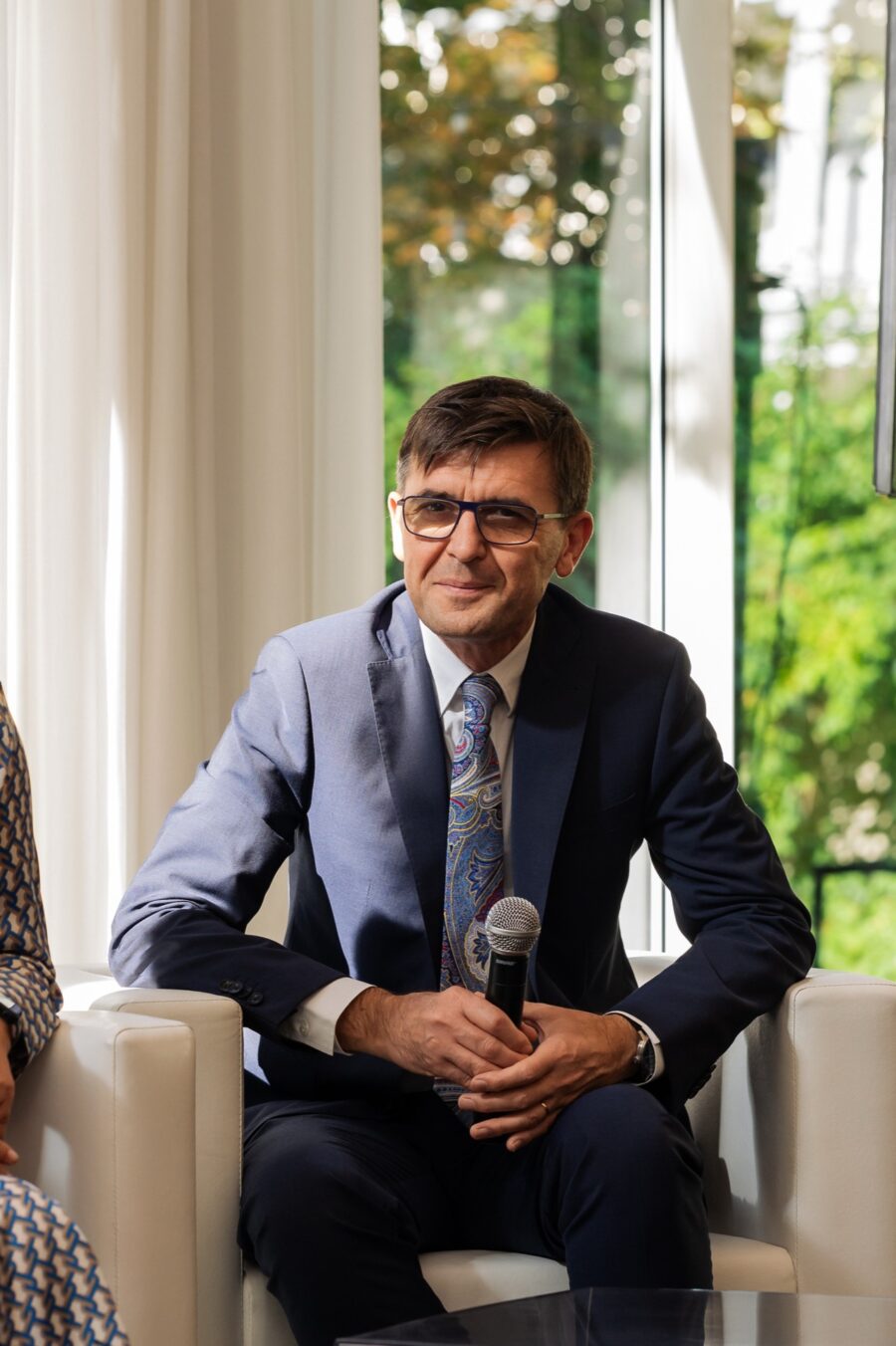 Portret panelisty z naturalnym uśmiechem, w tle zieleń ogrodu Villi Foksal