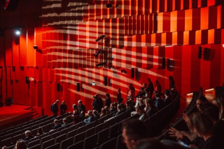 Duża sala audytoryjna z czerwonymi panelami akustycznymi, uczestnicy zajmują miejsca w rzędach