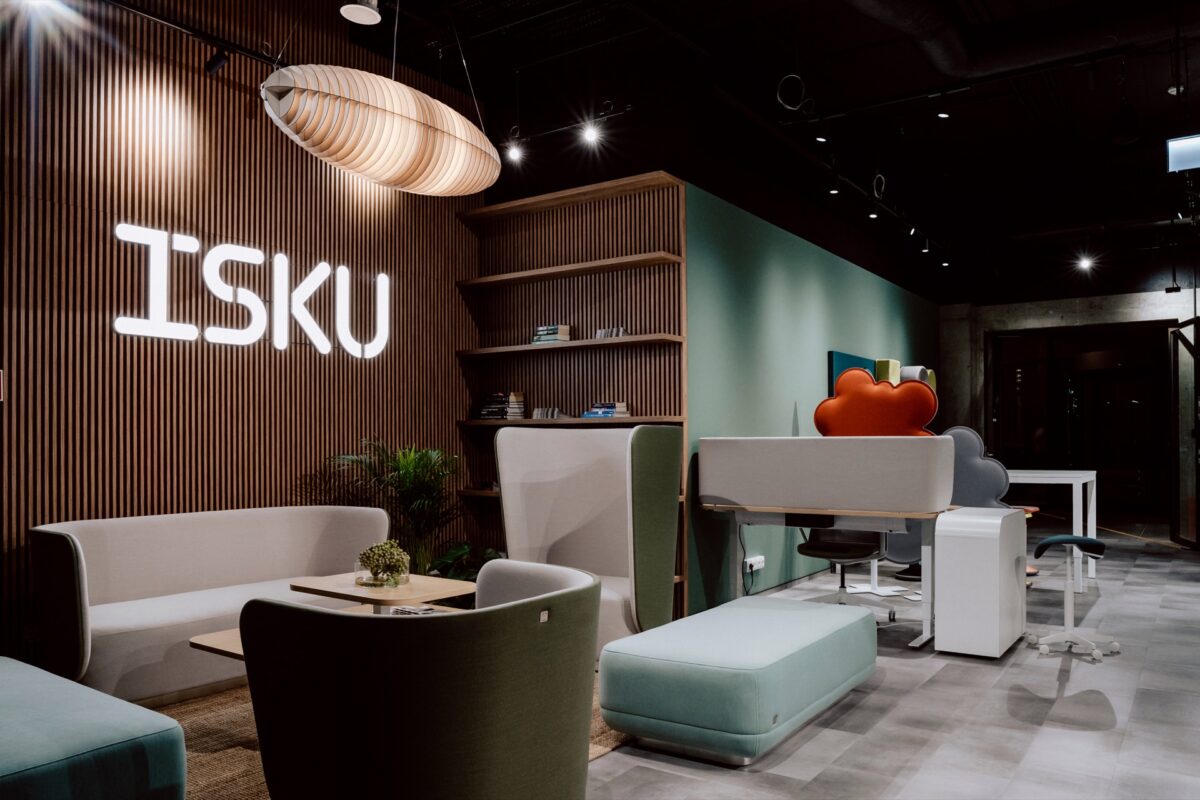 Strefa spotkań w showroomie ISKU pod logo marki, sofa z pufami i stanowiska pracy