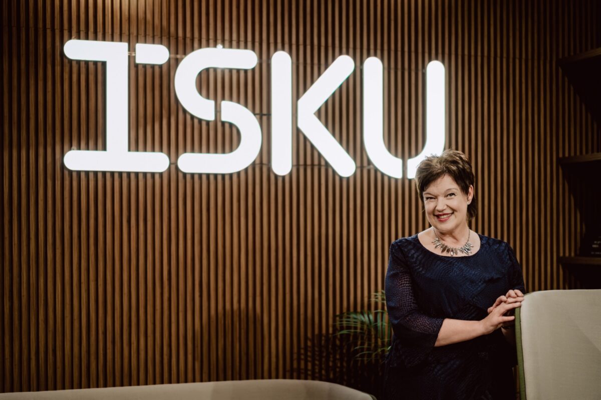 Gość wydarzenia przed logo ISKU na ścianie z drewnianych listew