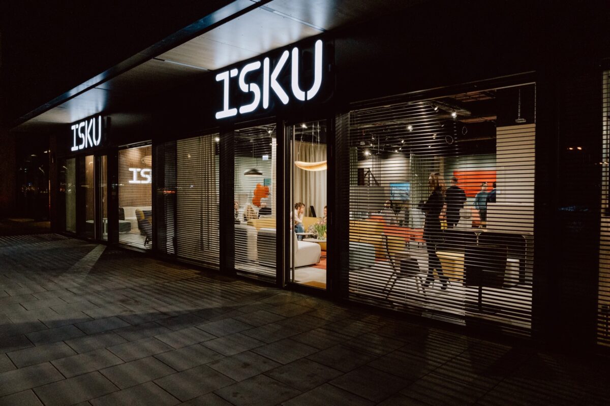 Showroom ISKU widziany z pasażu po zmroku, wnętrze z gośćmi za szybą