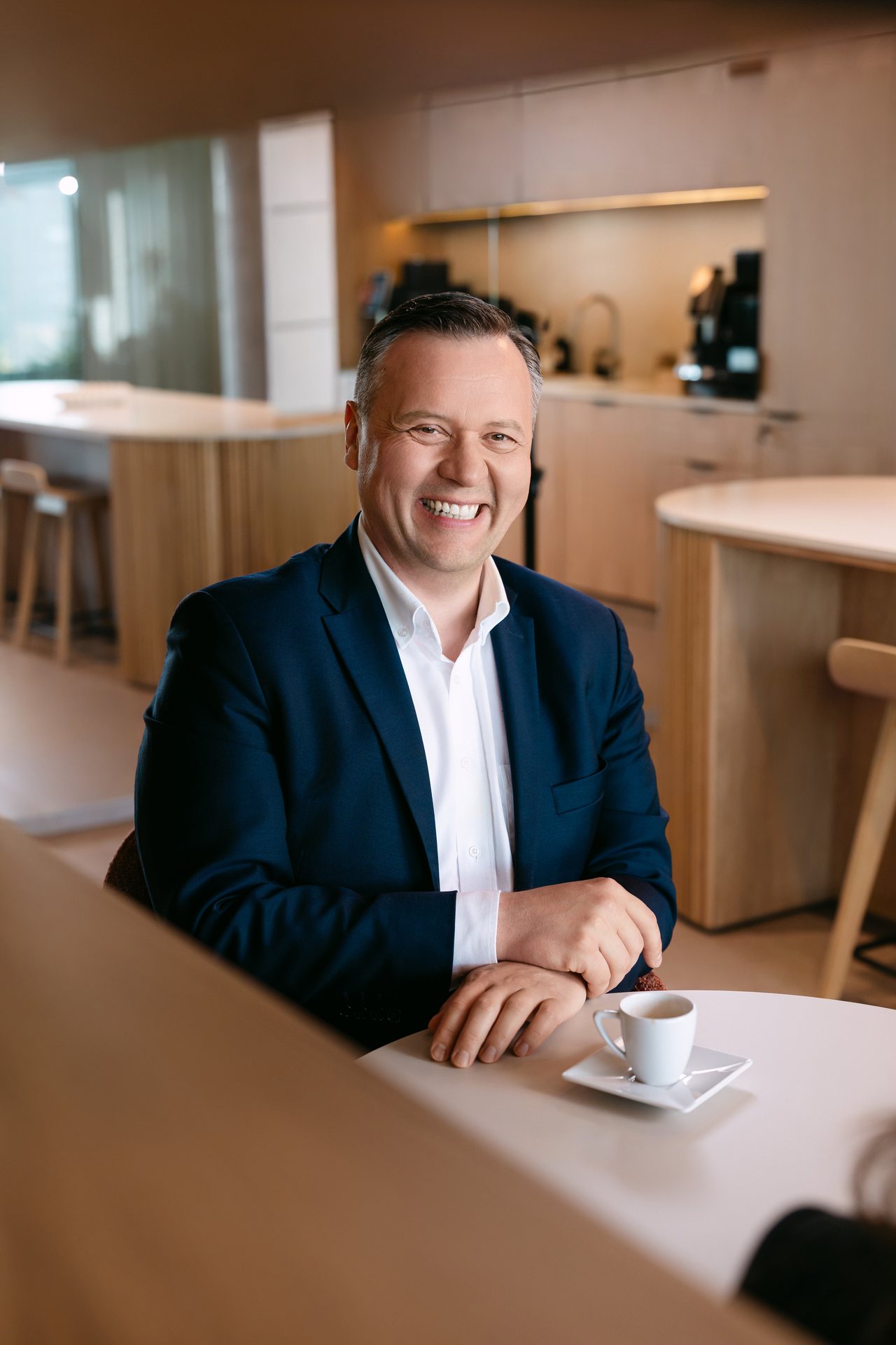 Porträt eines Mannes im dunkelblauen Sakko am Tisch im Firmenbüro, aufgenommen bei einem Business-Shooting.